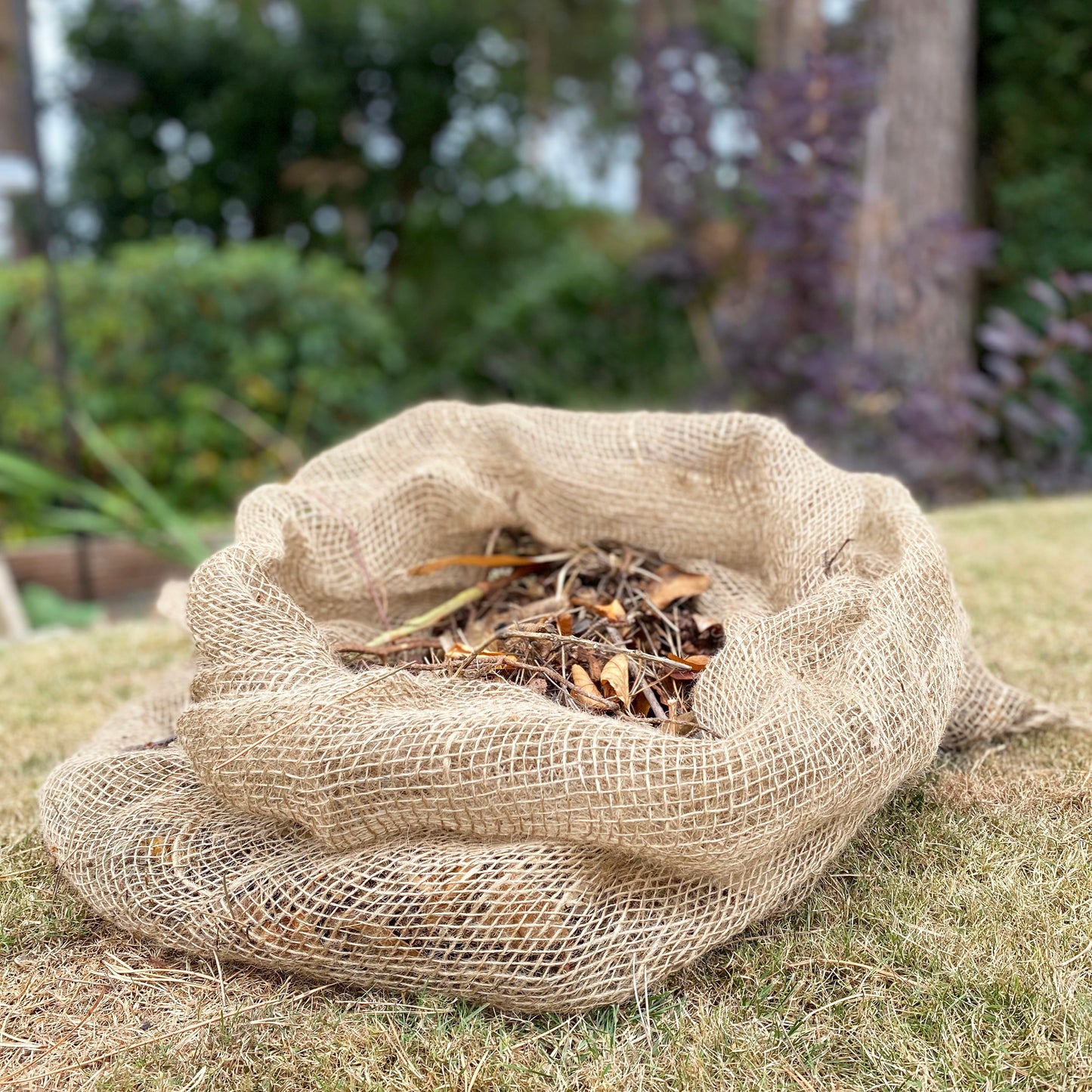 A burlap sack filled with leaves, placed on grass.