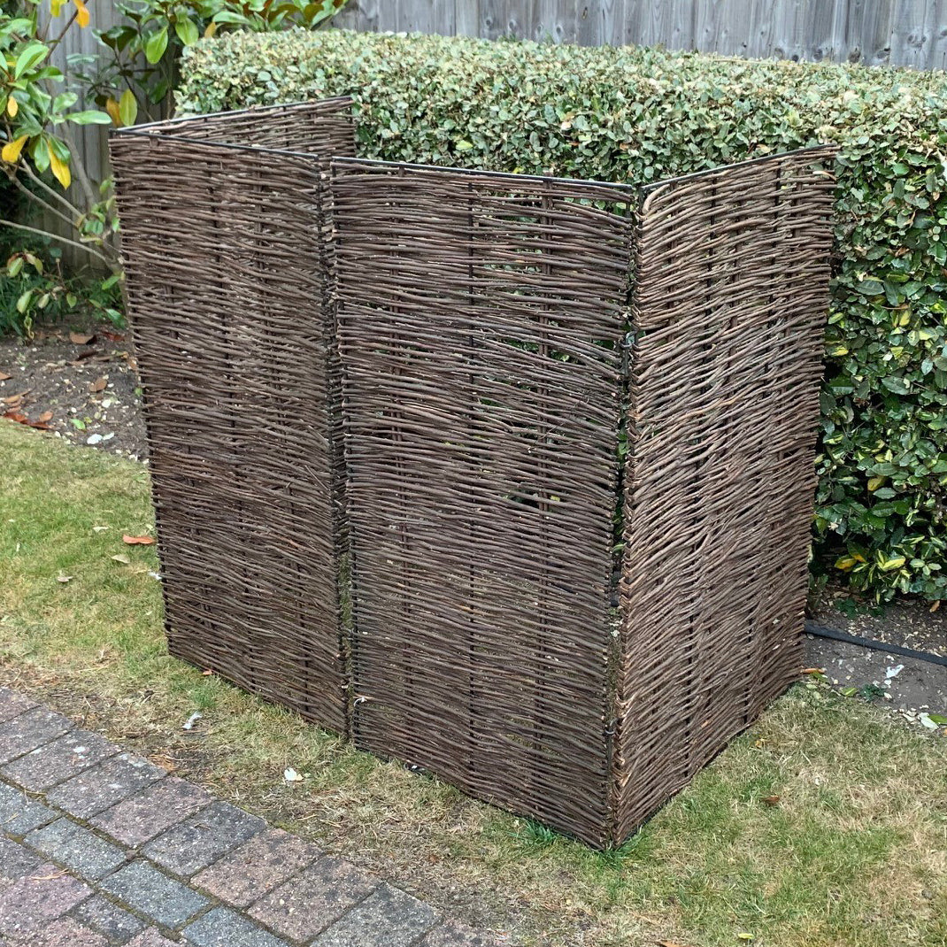 A double wheelie bin screen made of natural woven willow, with a strong metal framework, in a garden setting.