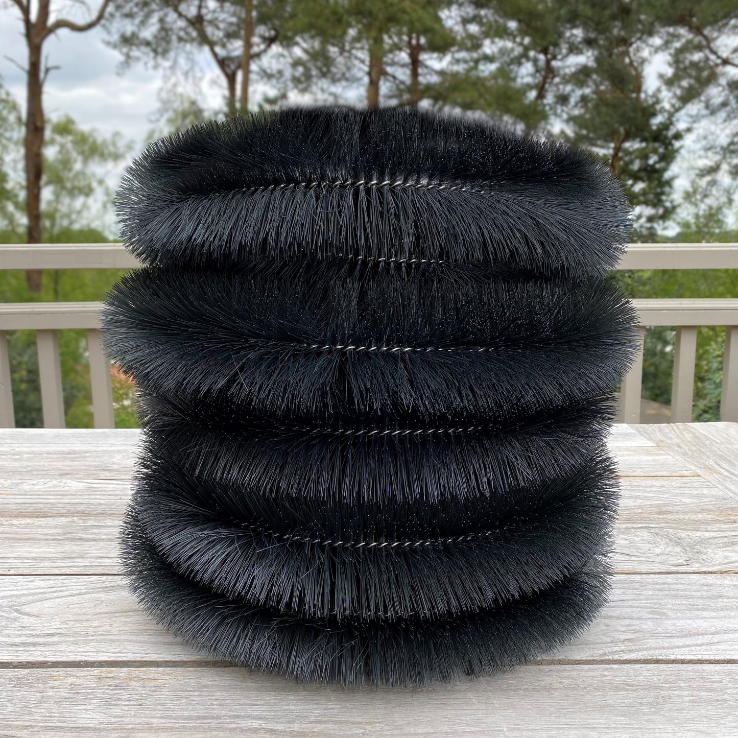 Stack of black feathered cylindrical objects gutter protection brush on a wooden surface with a blurred natural background