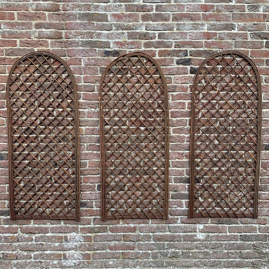 A set of three brown wooden trellises with a curved top design, mounted on a brick wall.