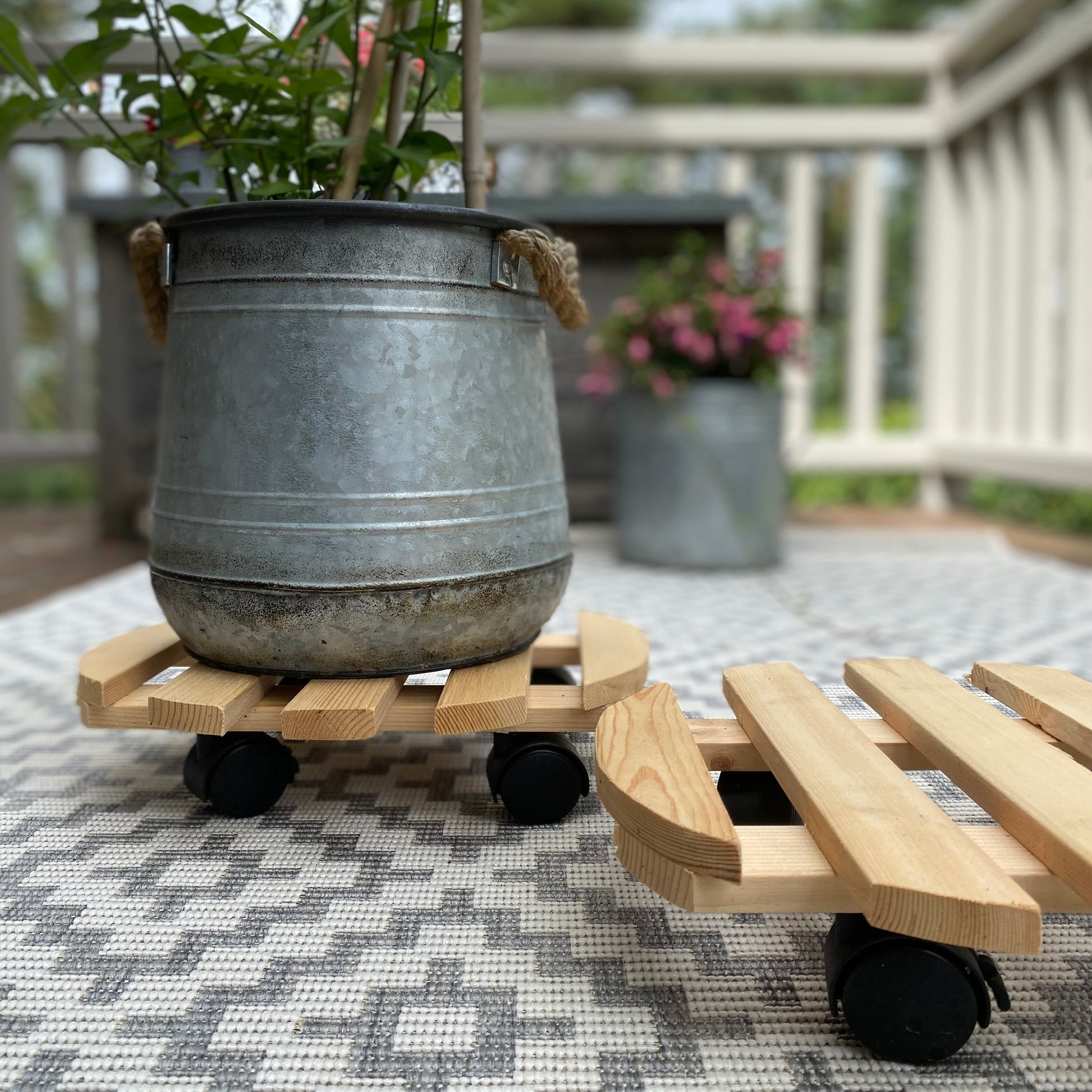 A wooden plant pot trolley mover designed to be used on wheels, with one braked wheel, displayed partially under a metal plant pot.