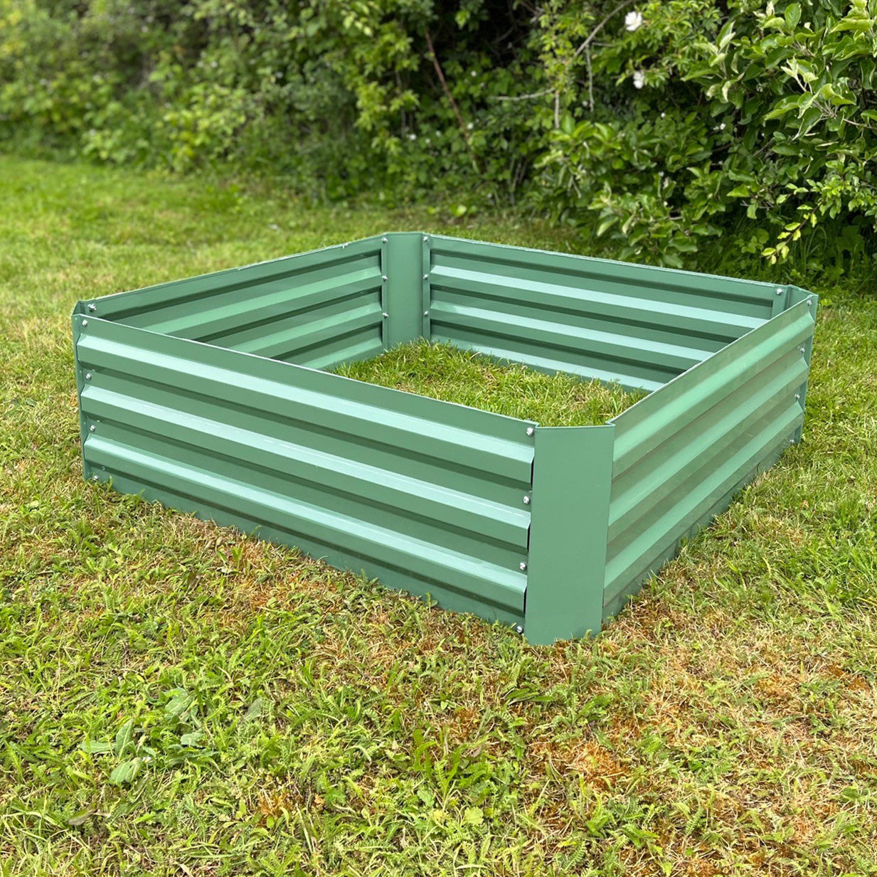 A green painted steel raised vegetable bed placed on grass.