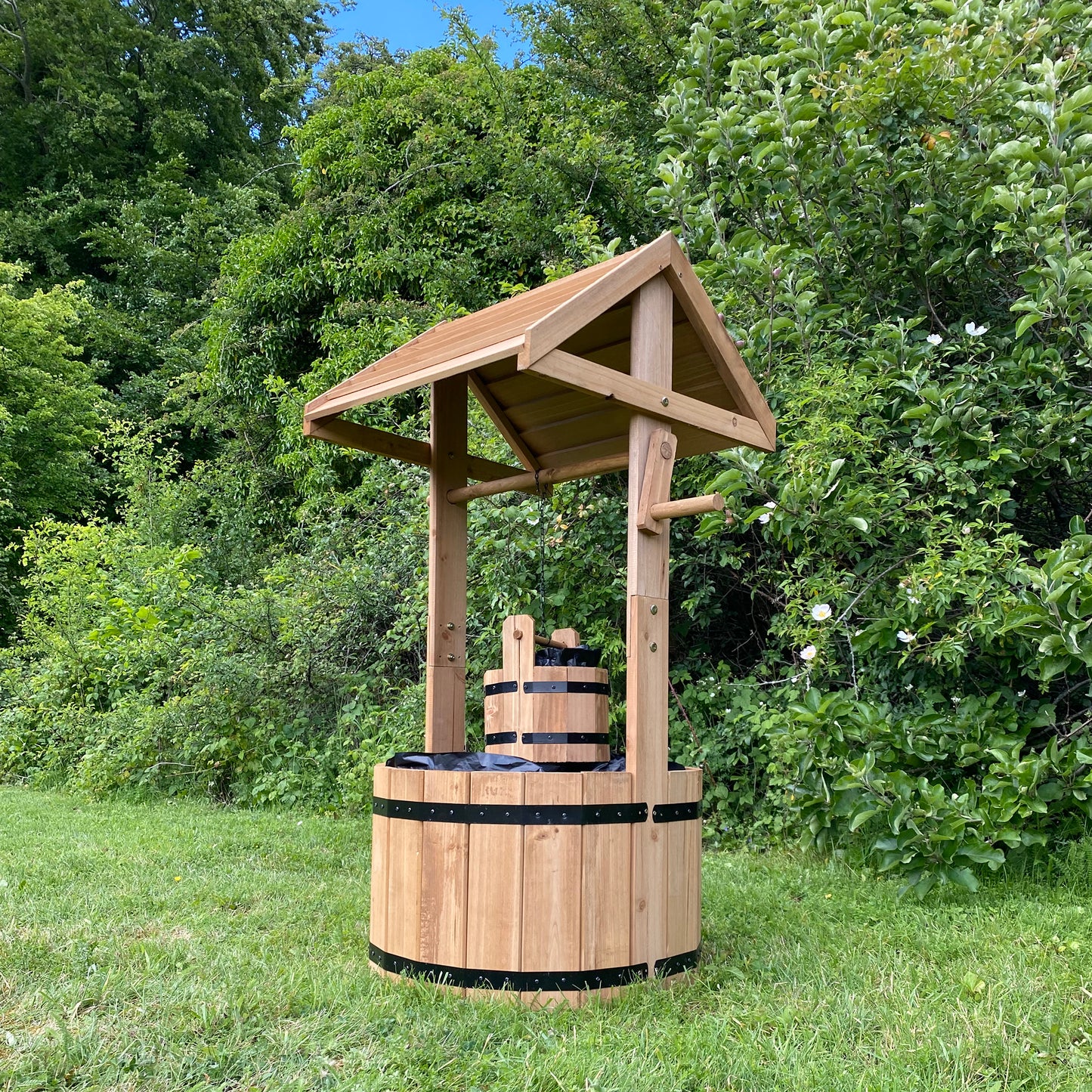 A wooden wishing well garden planter placed in a garden setting, featuring a rustic design with two planters.