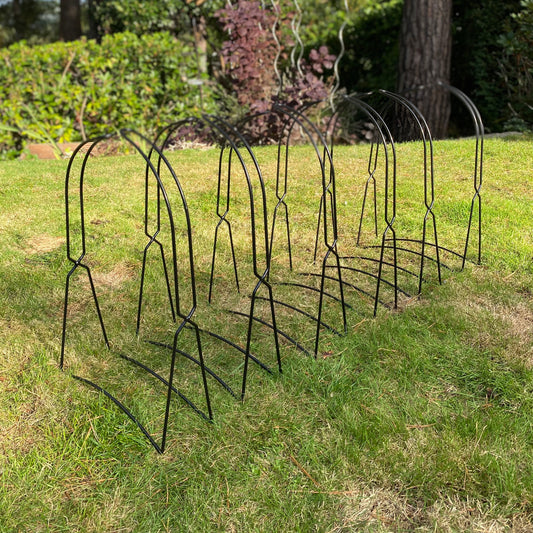 A set of six black, plastic-coated metal cane frame supports for growbags, displayed on grass.