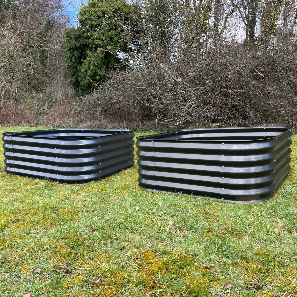 Two large metal raised vegetable beds in dark grey placed on grass, with visible corrugated metal sides and no plants.