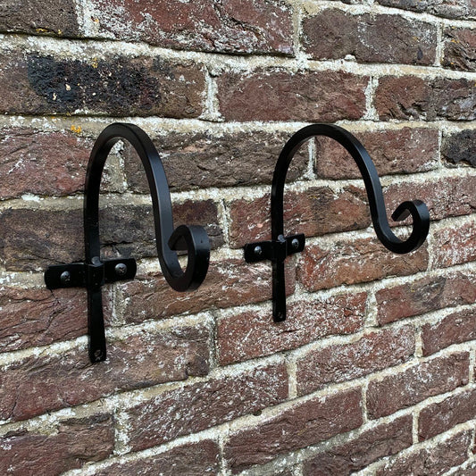 Two black metal round hanging basket hooks mounted on a brick wall.