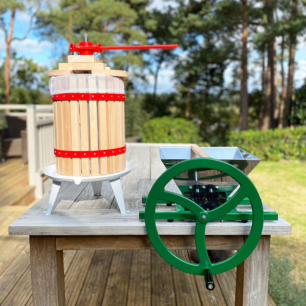 A traditional styled 18 litre fruit press with a manual apple scratter, both made of wood and metal, placed on a table outdoors.