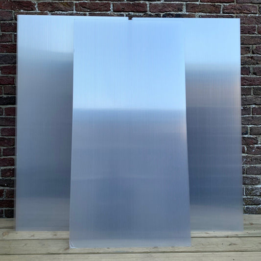 Stack of clear polycarbonate sheets leaning against a brick wall.