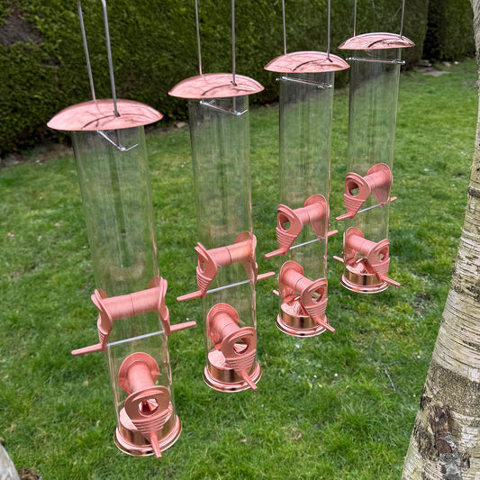 A set of four copper color bird seed feeders with retractable hanging hooks and detachable feeding ports, displayed on grass.