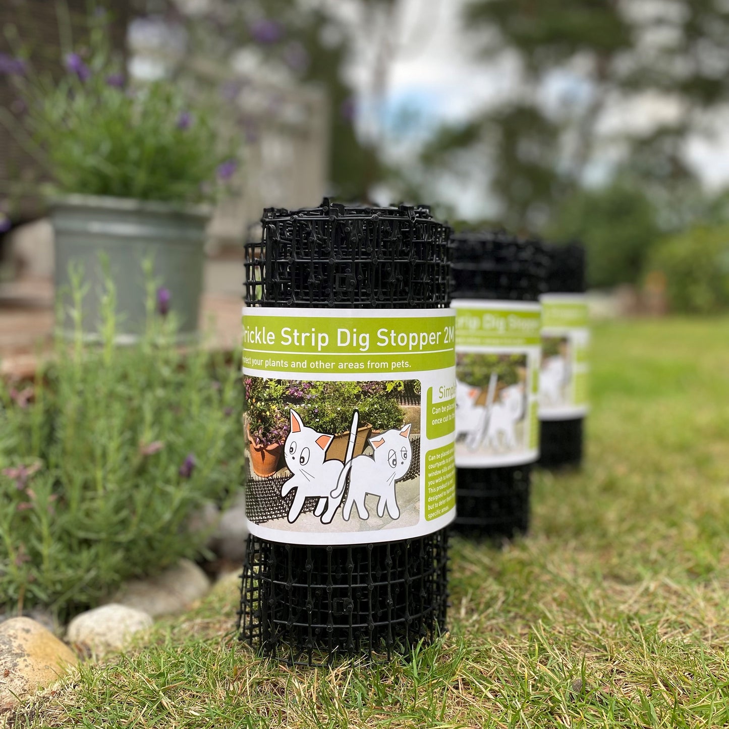 Three rolls of black plastic plant prickly strip dig stopper designed to deter pets from flowerbeds, displayed on grass against a gardening background.