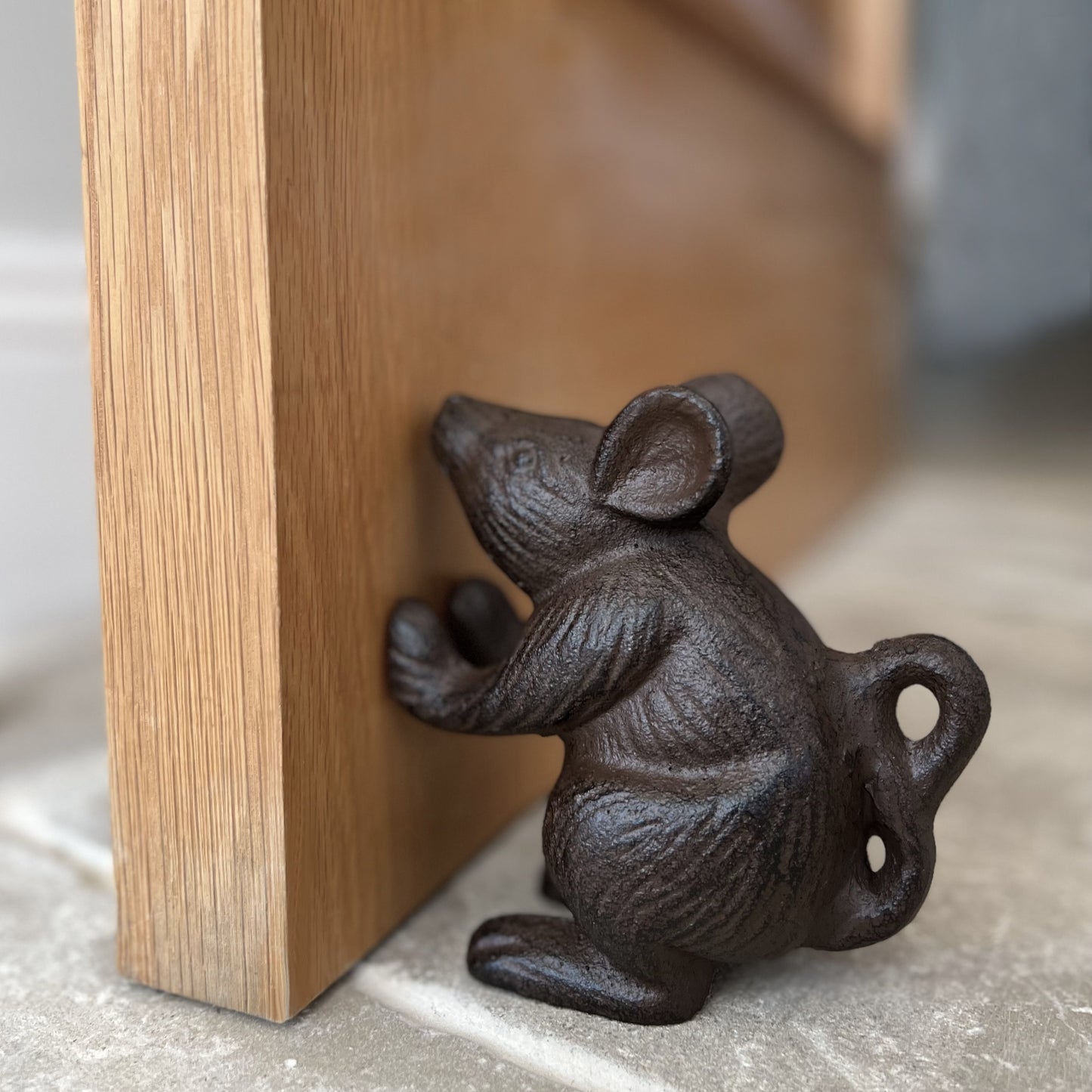 A cast iron doorstop shaped like a mouse, with a vintage brown finish, holding a door open.