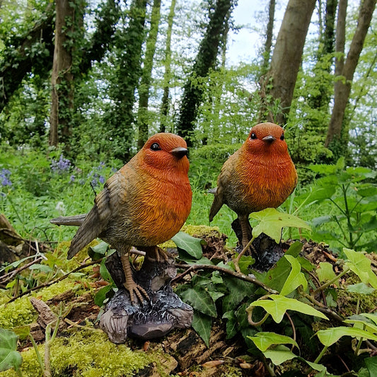 A pair of hand painted resin garden ornaments depicting two robins perched on a tree stump, set against a natural background with green foliage.