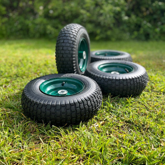 A set of four garden trolley replacement wheels placed on grass. Each wheel has a green rim with a black tire.