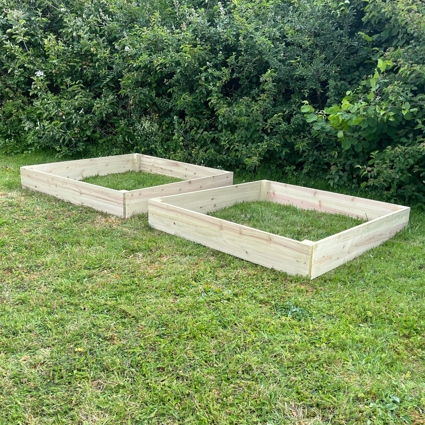 Two wooden raised vegetable beds placed on grass against a shrubbery background.