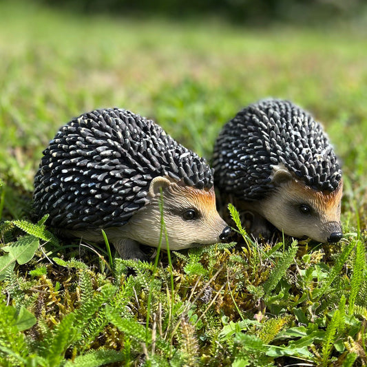 Two resin garden ornaments shaped like baby hedgehogs with black, white, and grey spiky coats, placed on green grass.