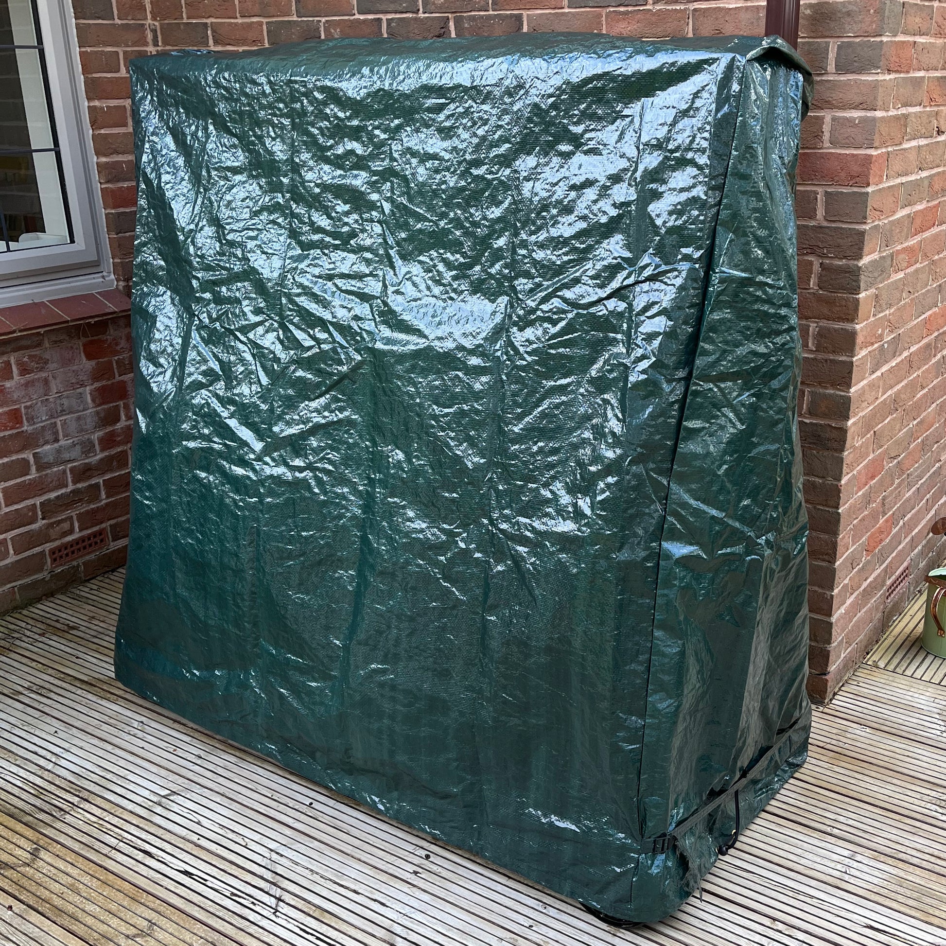 A green waterproof table tennis table cover fitted over a table, placed on an outdoor patio.