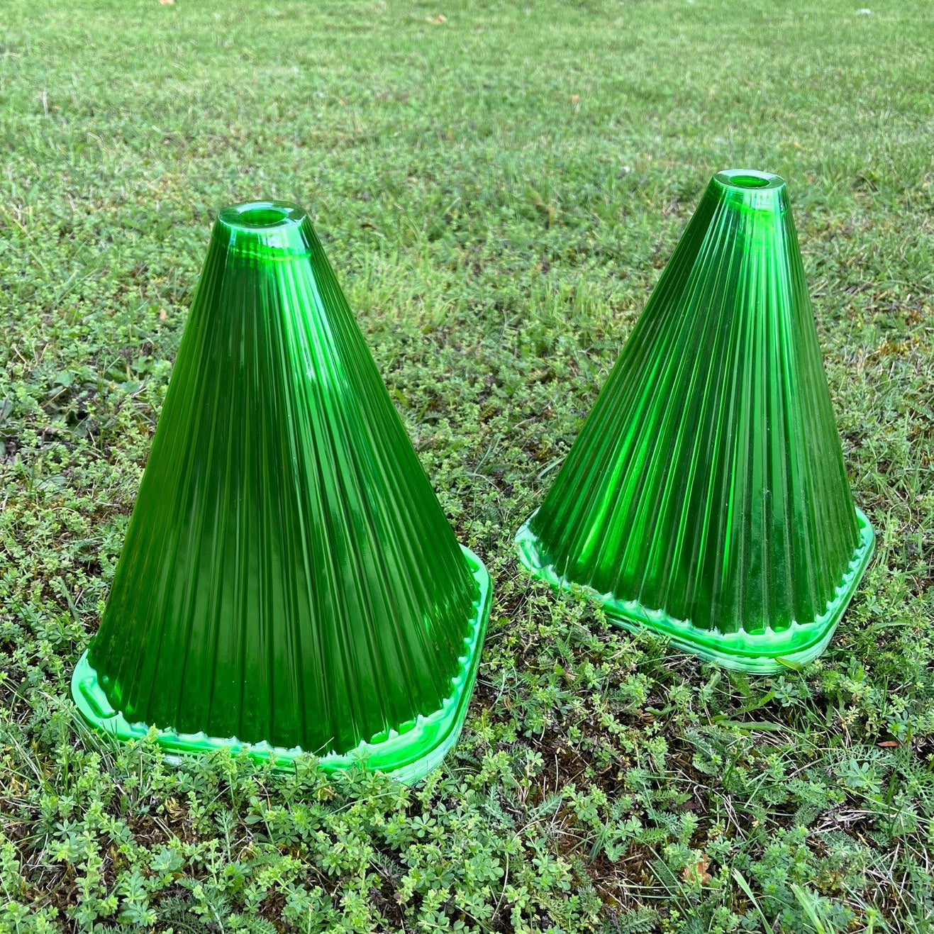 Two green plastic plant protection cloche covers placed on a grass surface.
