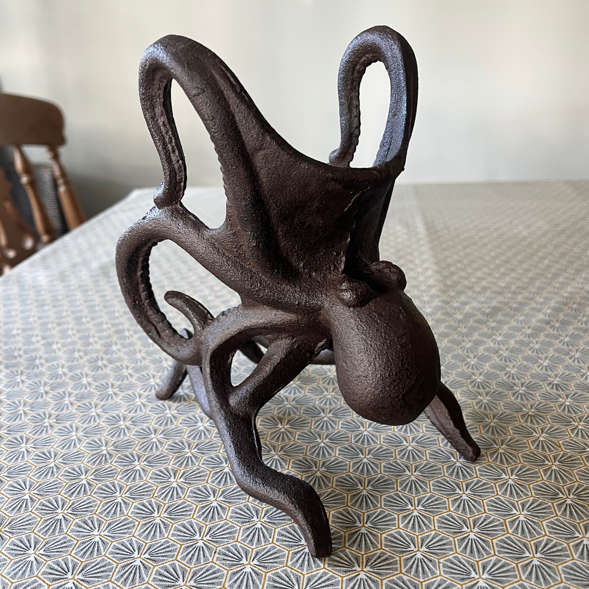 A black cast iron wine bottle holder shaped like an octopus, displayed on a patterned surface.