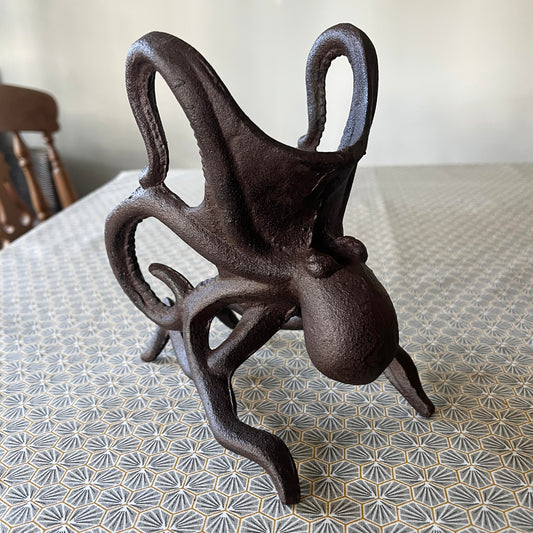 A black cast iron wine bottle holder shaped like an octopus, displayed on a patterned surface.