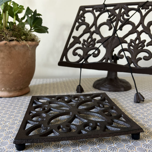 A traditional cast iron ornate cookbook stand and square trivet set, displaying an ornate floral pattern with a natural, rustic finish.