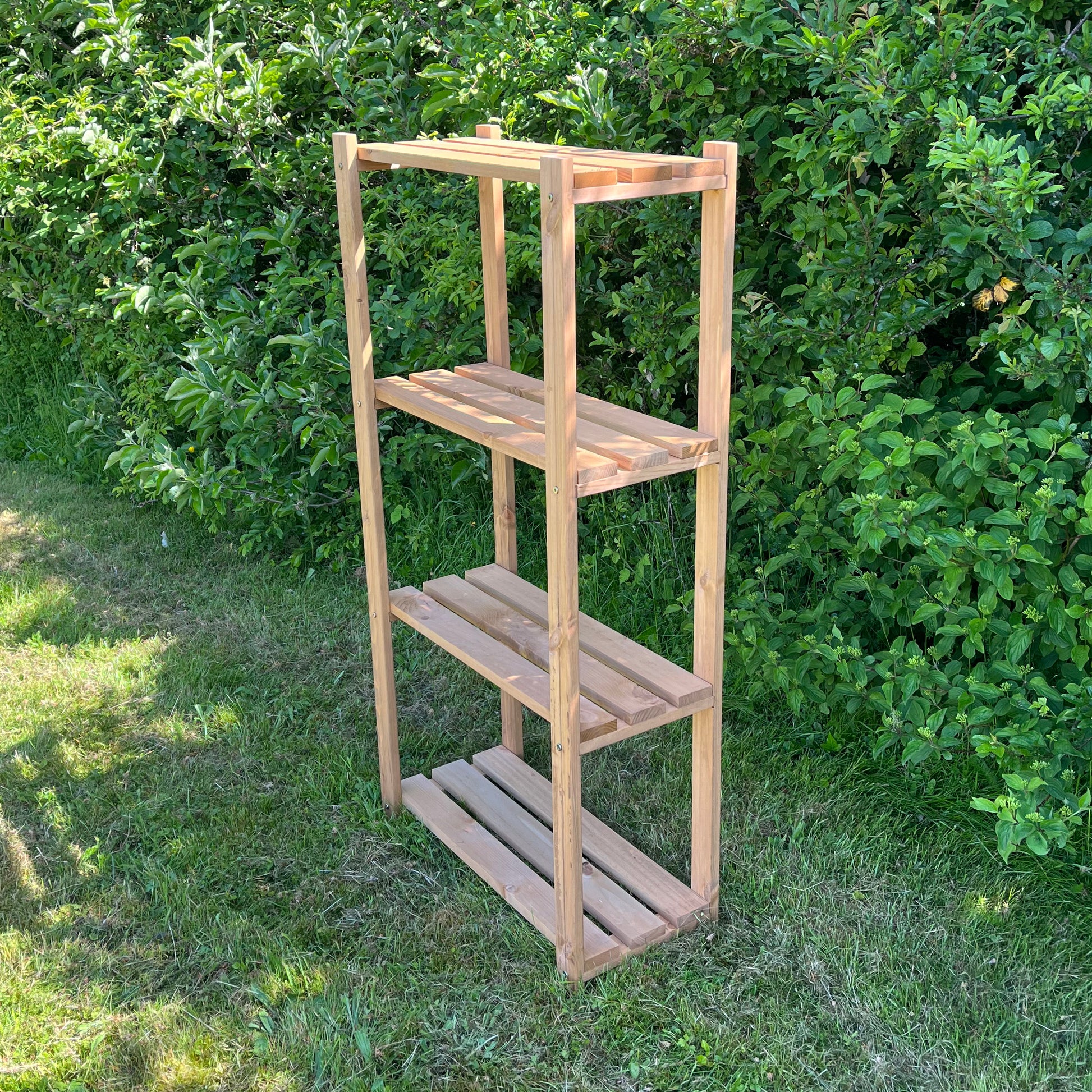 A 4-tier wooden shelving storage rack placed outdoors with a green hedge in the background.