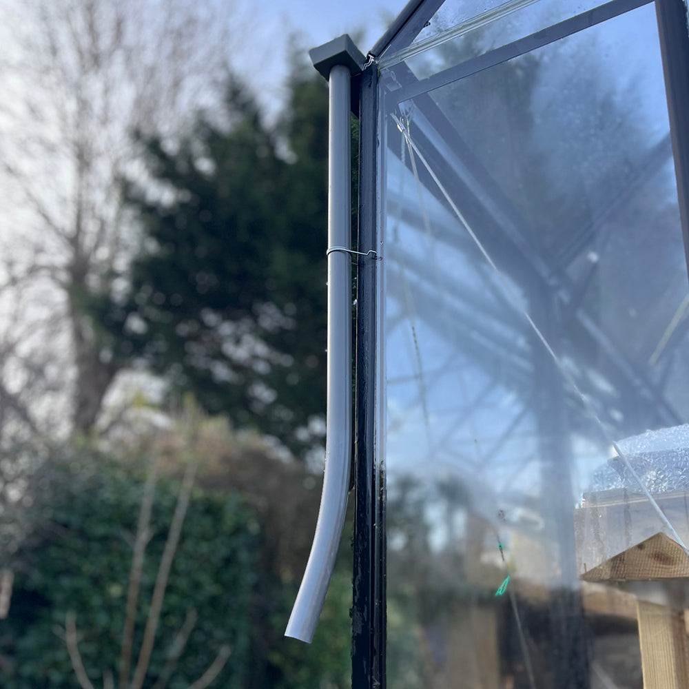 A grey gutter downpipe attached to a greenhouse, designed to channel rainwater into a water butt.