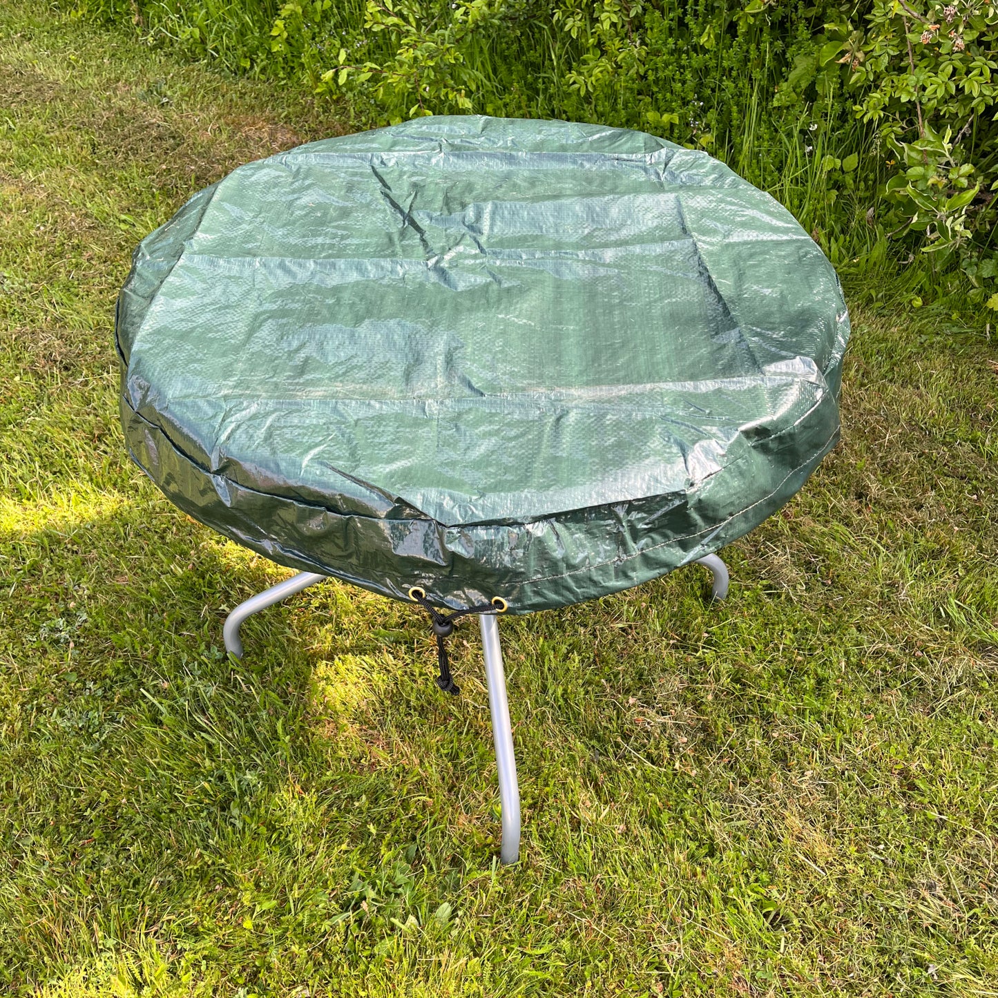 A green round garden table top cover fitted on a table, placed outdoors on grass.
