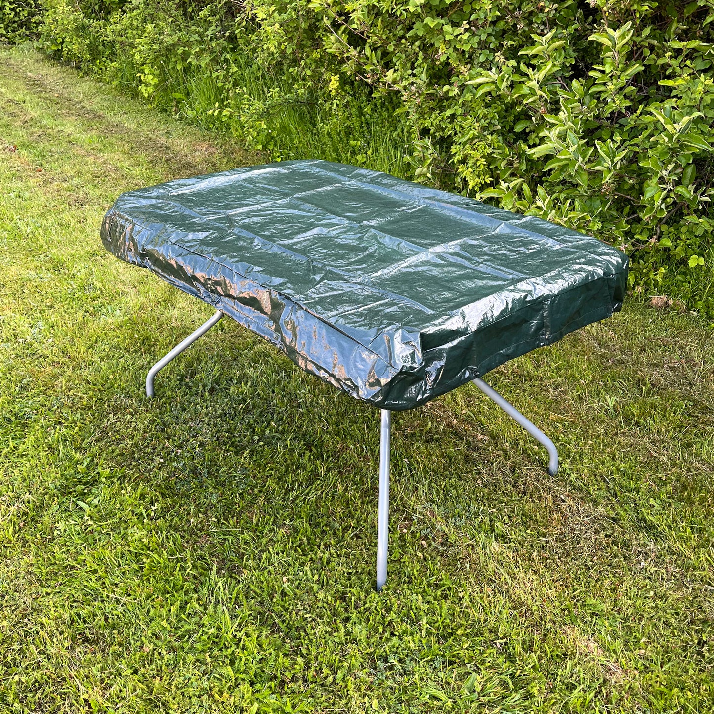A green waterproof rectangular table top garden furniture cover fitted on a table outdoors.