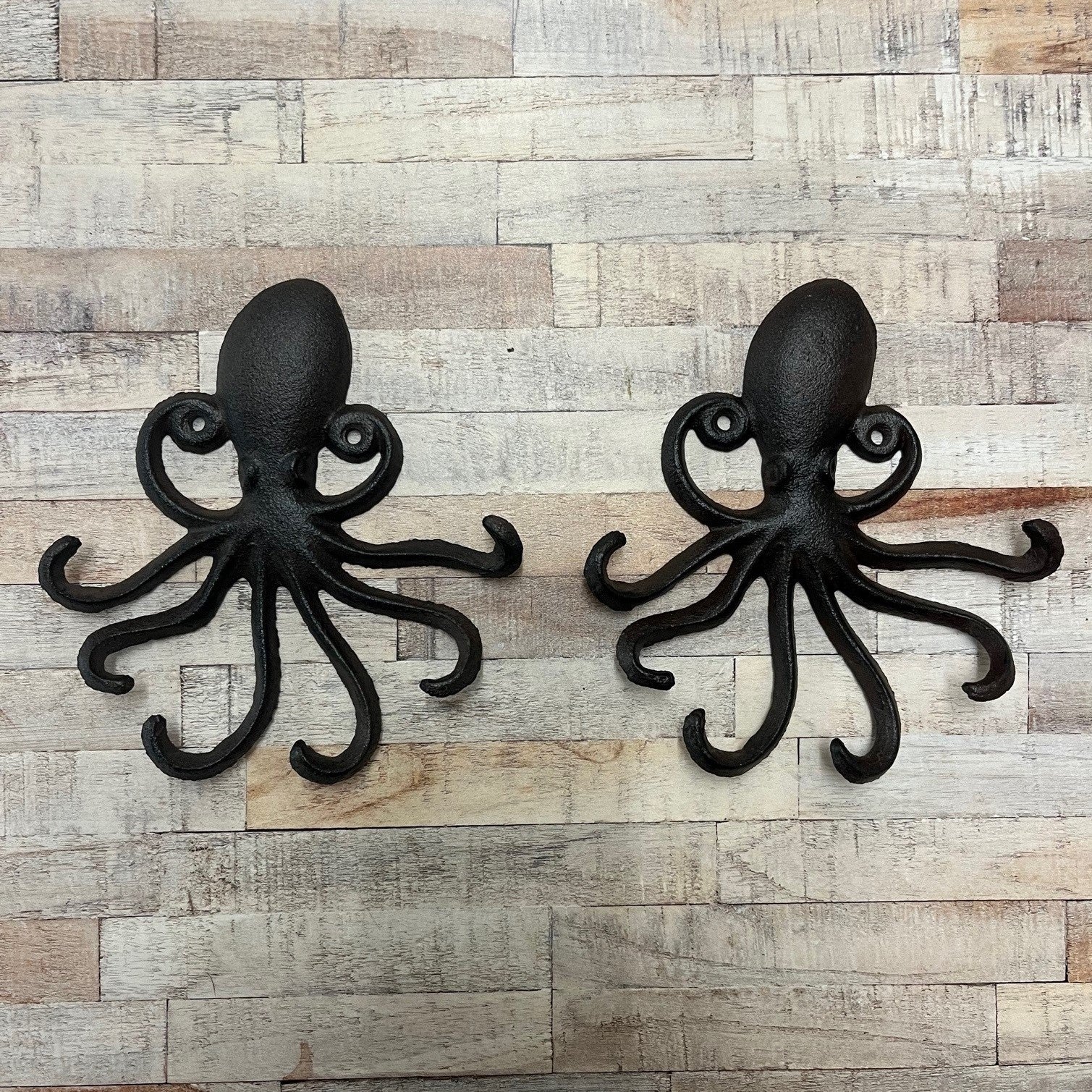 Two black cast iron octopus wall hook racks mounted on a wooden wall.