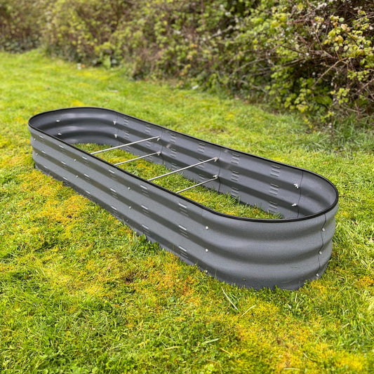 A large metal oval raised vegetable bed in dark grey color, placed on a grassy surface.