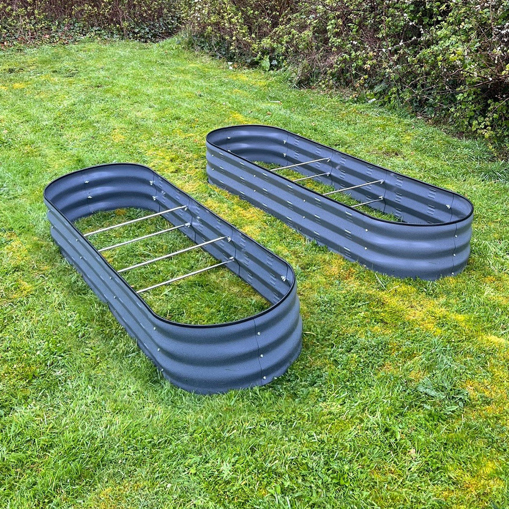 Two large metal oval raised vegetable beds in dark grey, placed on a grass surface.