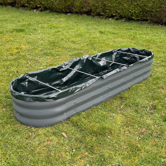 A green liner for an oval metal raised vegetable bed laid on grass.