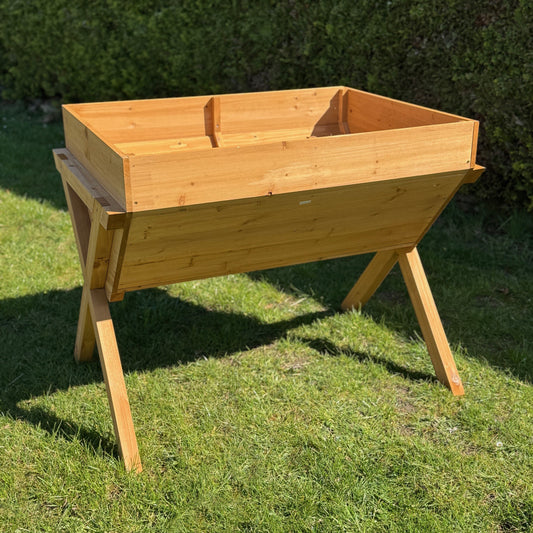 A wooden raised vegetable bed planter placed on grass, with a sunny shadow cast across its surface.