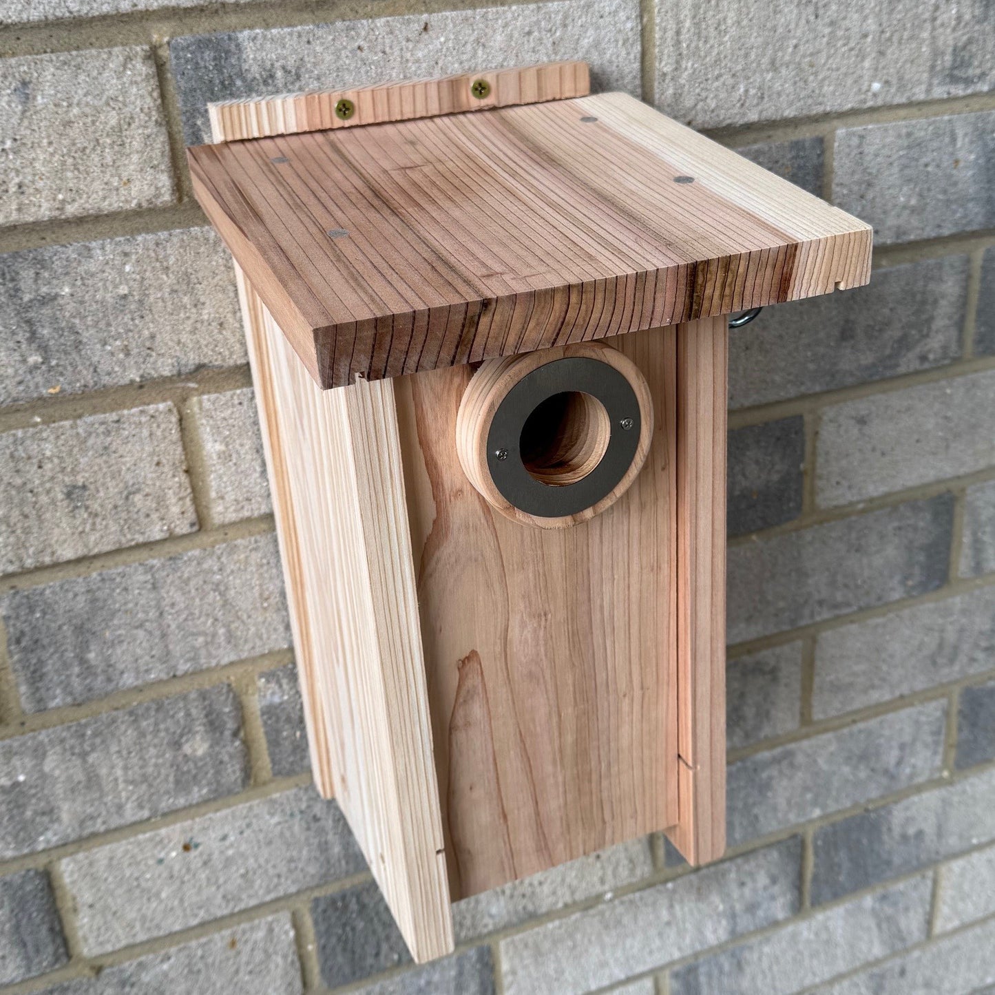 A wooden birdhouse with a circular entrance hole, mounted on a brick wall.