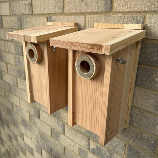 Two wooden birdhouses mounted on a brick wall, each with a round entrance hole and secured by metal screws.