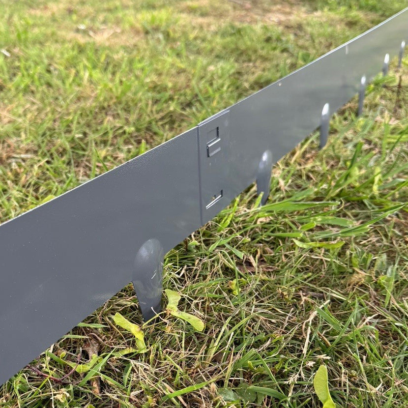 A set of grey metal garden lawn and border edging panels installed on grass, showing the interlocking mechanism and spiked feet.