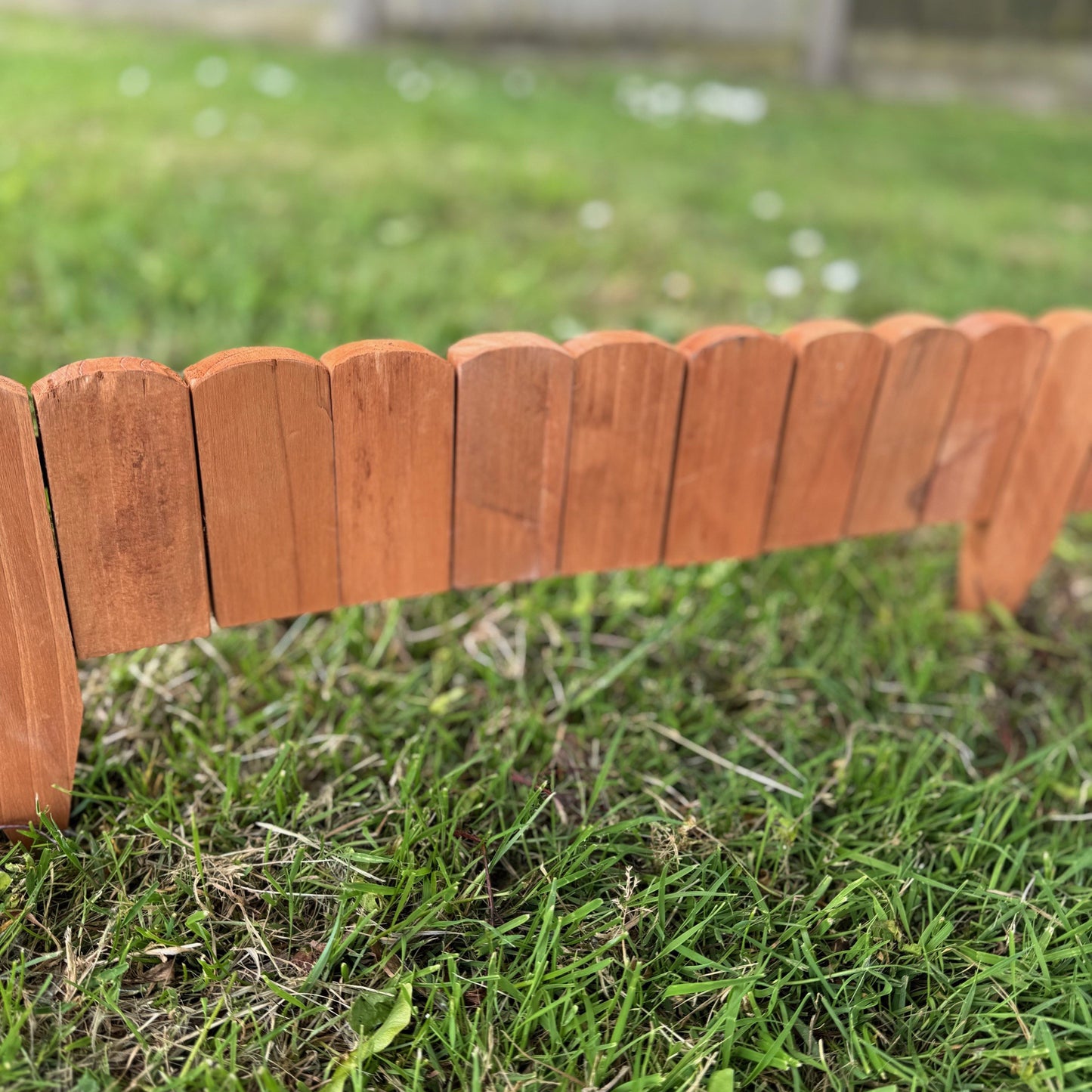 A series of brown wooden log roll style lawn edging panels arranged on a grassy surface.