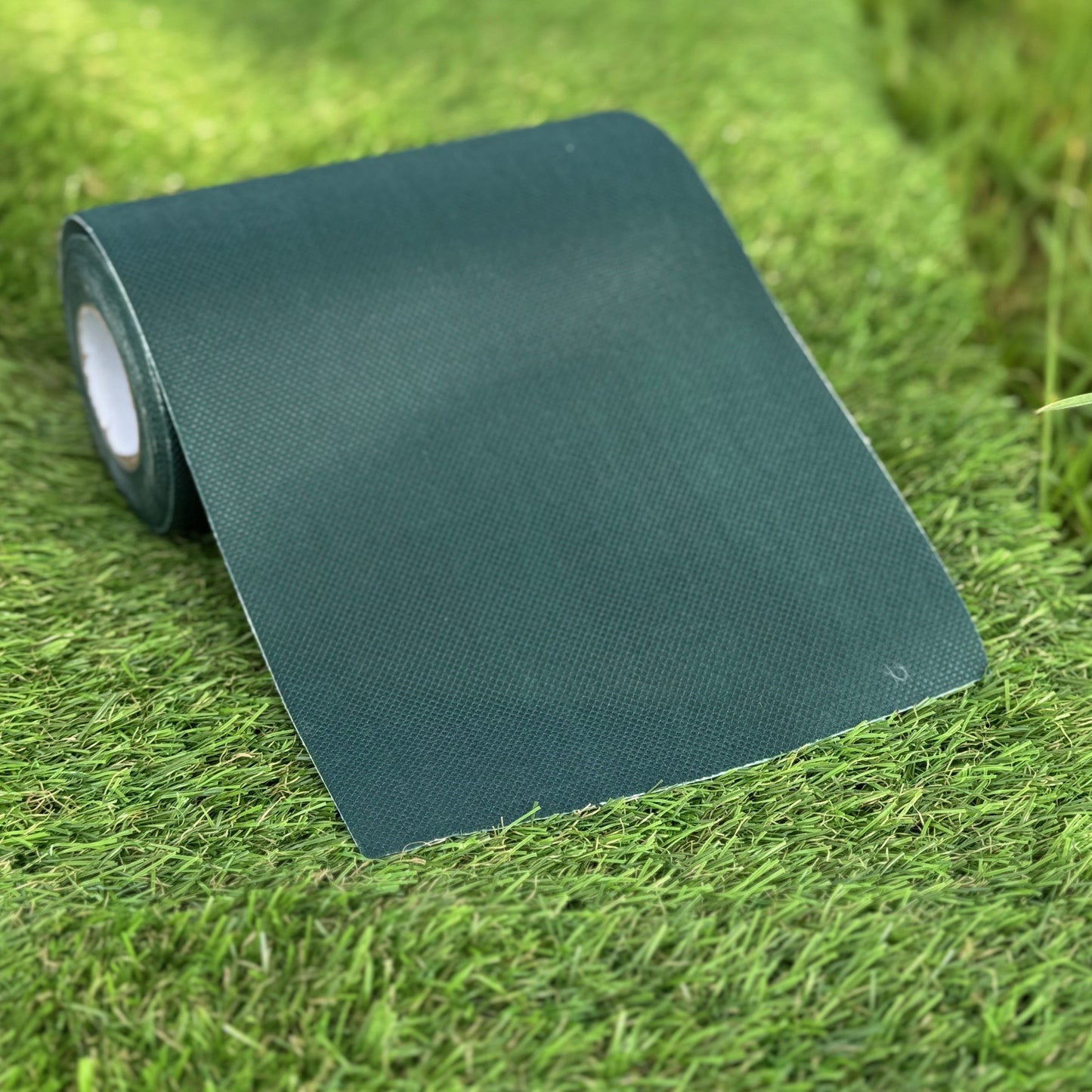 A roll of green artificial grass adhesive joint tape laid out on more artificial grass.