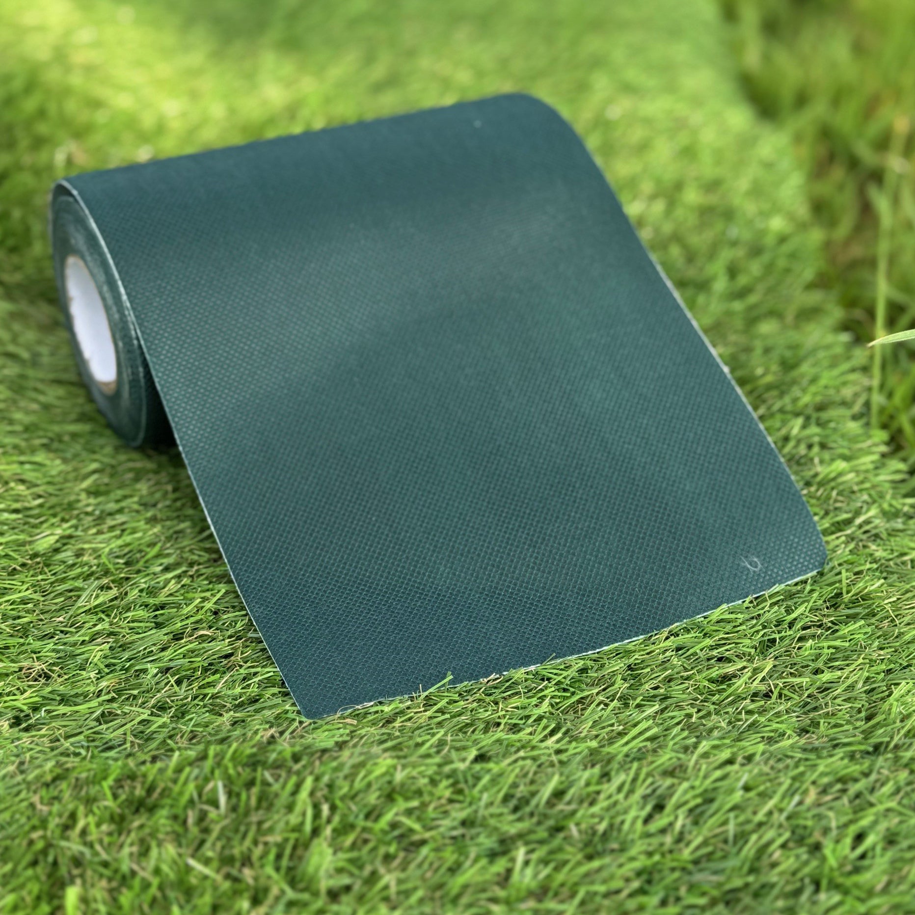 A roll of green artificial grass adhesive joint tape laid out on more artificial grass.