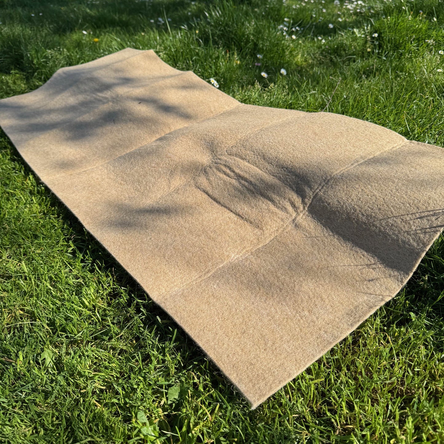 A beige jute garden hanging basket liner laid out on a grass surface.