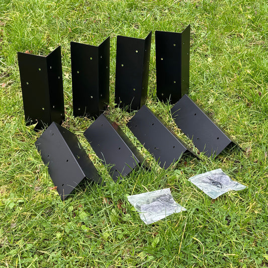 A pack of eight black metal raised vegetable bed corner brackets laid on grass with some packaging visible.