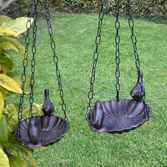 Two cast iron bird baths hanging on chains with a grass background.