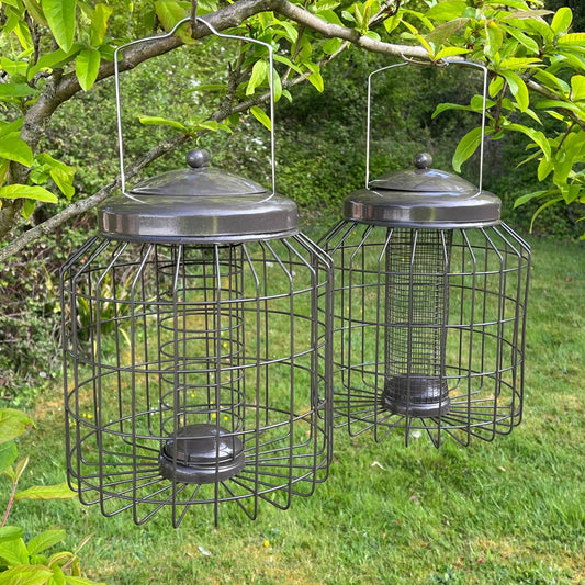 Two squirrel proof hanging bird feeders in gun metal grey color, with a mesh cage design and a lid on top.