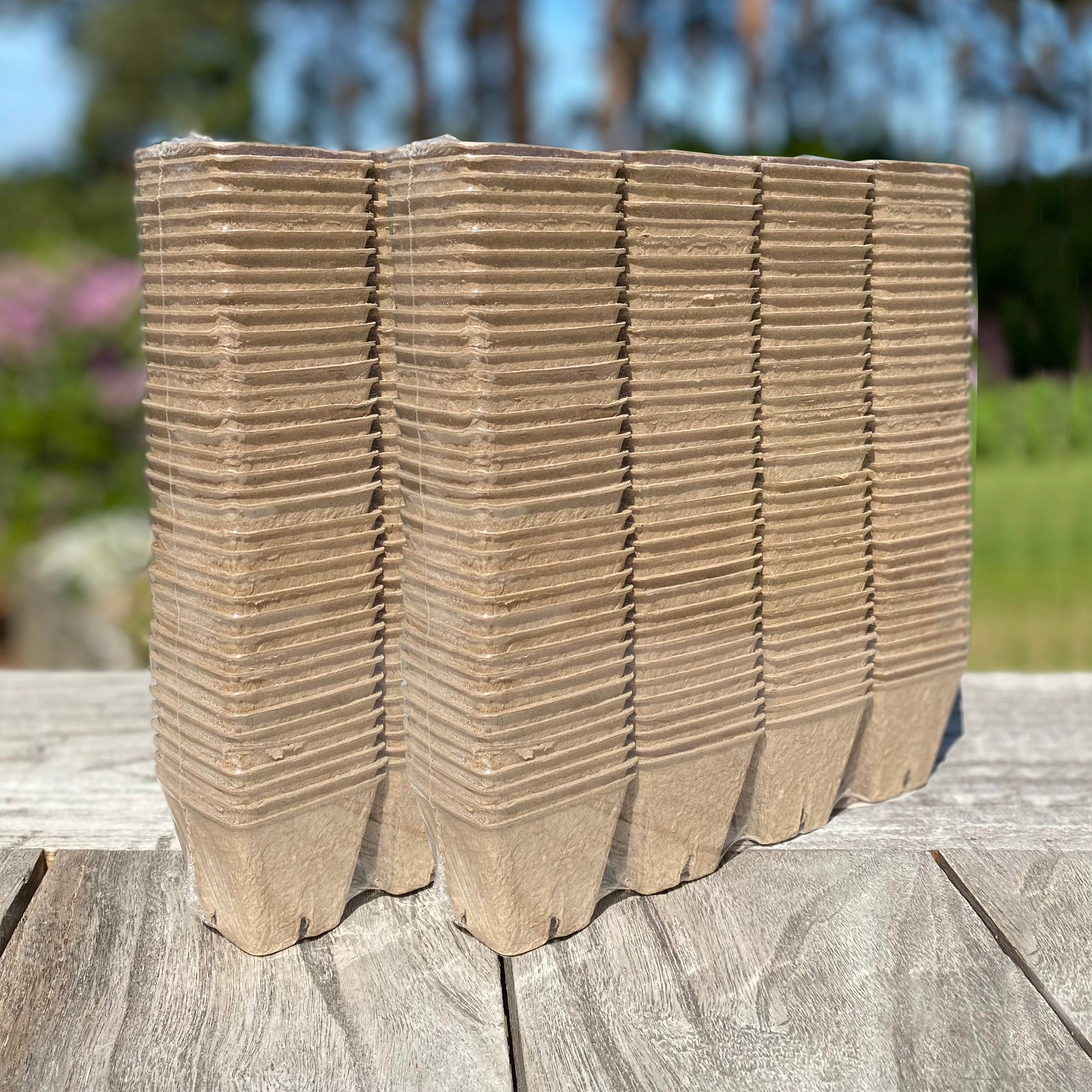 A stack of square, brown eco-friendly fibre biodegradable and compostable plant pots outdoors on a wooden surface.