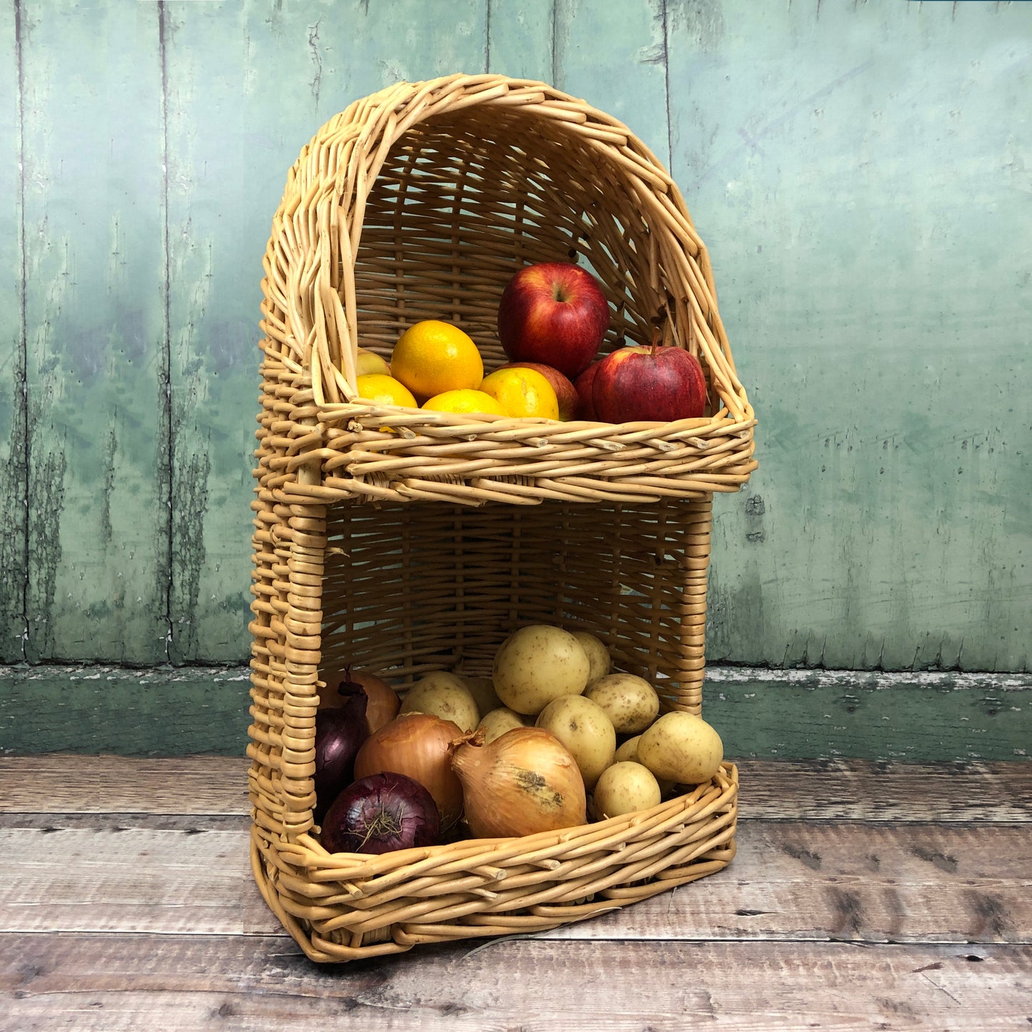 A hand woven willow storage basket filled with fruits and vegetables, displayed against a wooden backdrop.