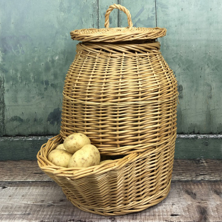 A hand woven wicker potato storage hopper with a removable lid, containing potatoes, displayed against a wooden background.