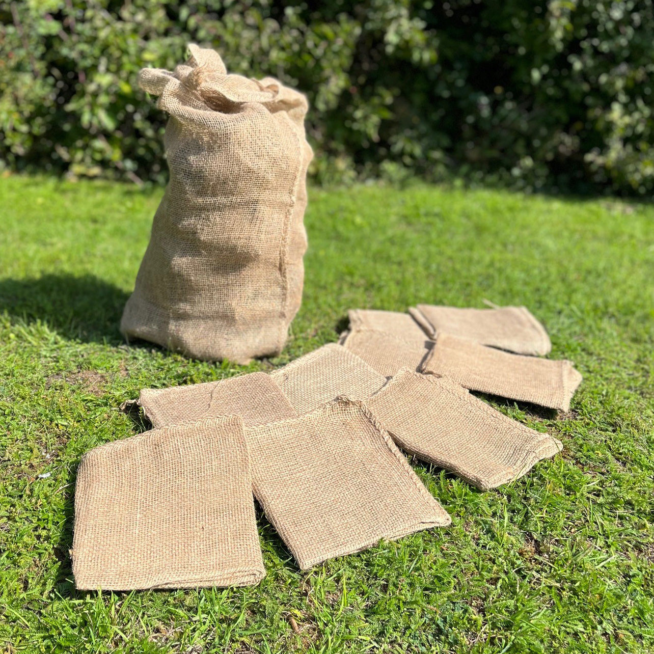 A beige jute sack laid out on grass, with additional folded sacks nearby.