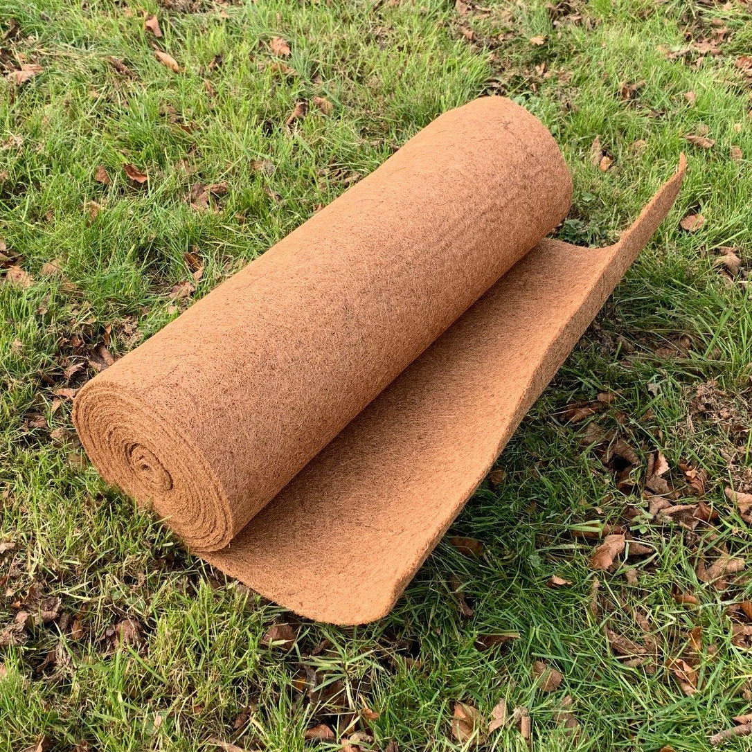A rolled up brown coconut fibre liner for planters placed on a grassy surface.
