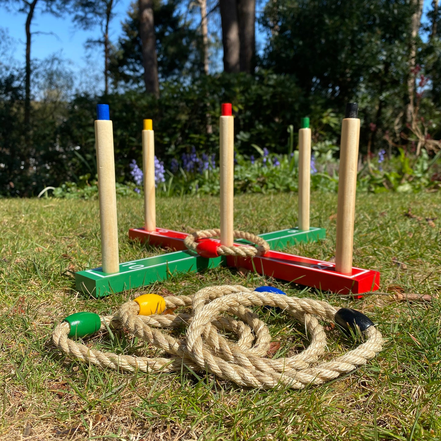 A traditional garden ring toss game set up on grass, consisting of wooden posts with colored tops and rope hoops.