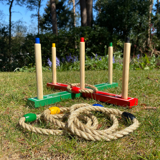 A traditional garden ring toss game set up on grass, consisting of wooden posts with colored tops and rope hoops.